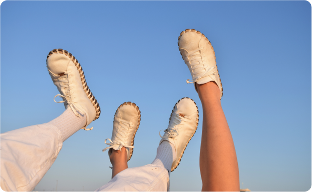 Two sets of feet dangling upward toward the sky while wearing white sneakers