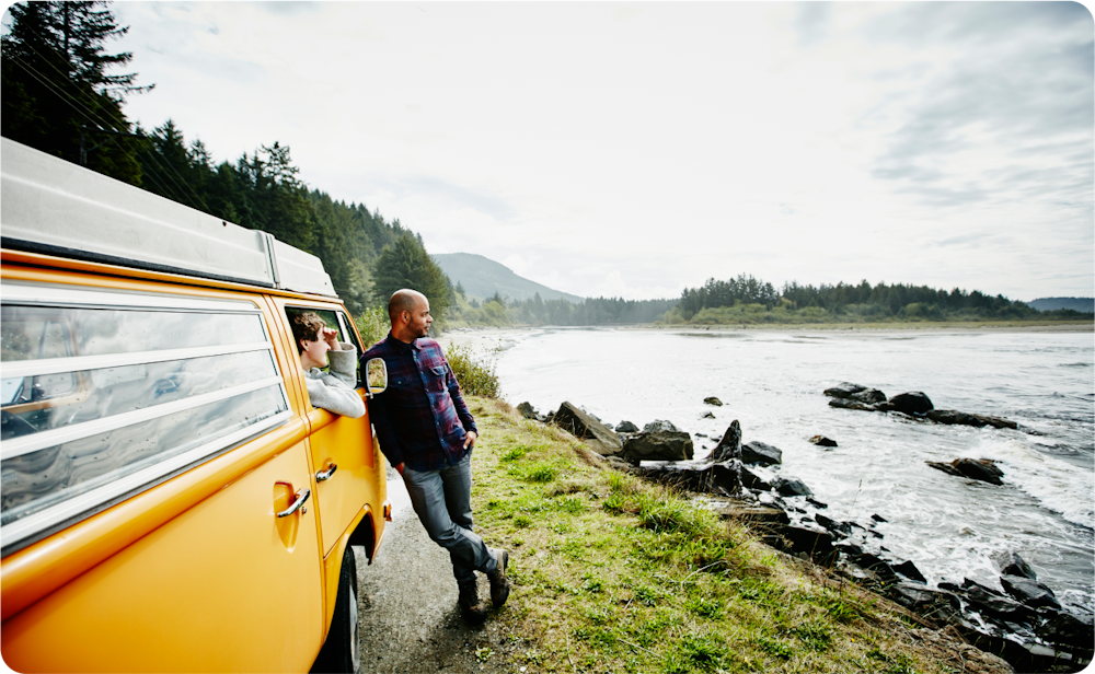 Decorative image of two people by a yellow van looking out over a beautiful lake and sunny landscape