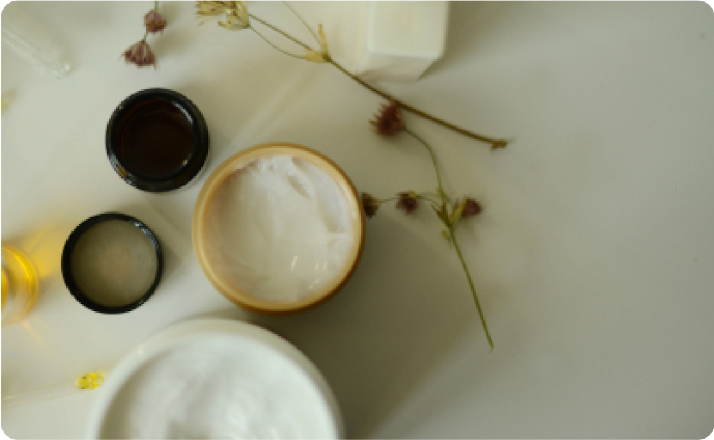 Ecommerce image of various body creams and containers with flowers against a flat lay